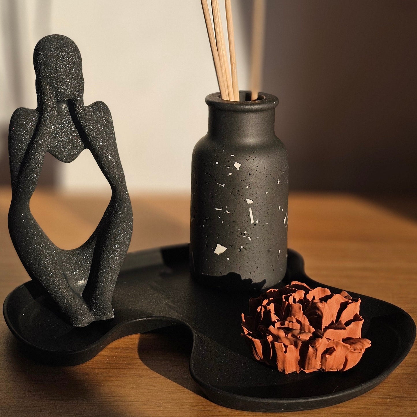 Apportez une touche de raffinement à votre intérieur avec ce set décoratif en jesmonite noire de la Collection Élégance. Un ensemble minimaliste et harmonieux, composé d’un plateau noir, d’un flacon terrazzo et d’une fleur parfumée couleur terracotta.